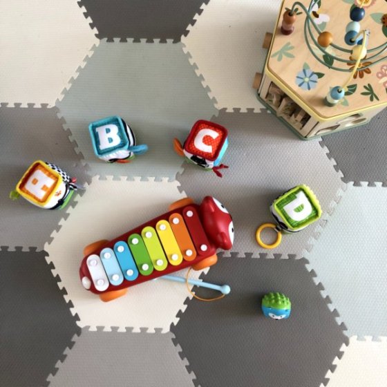 Cubes en tissu de différentes couleurs affichant chacun une lettre de "A" à "D", un xylophone arc-en-ciel en forme de renard et un cube d'activité sur un tapis de jeu